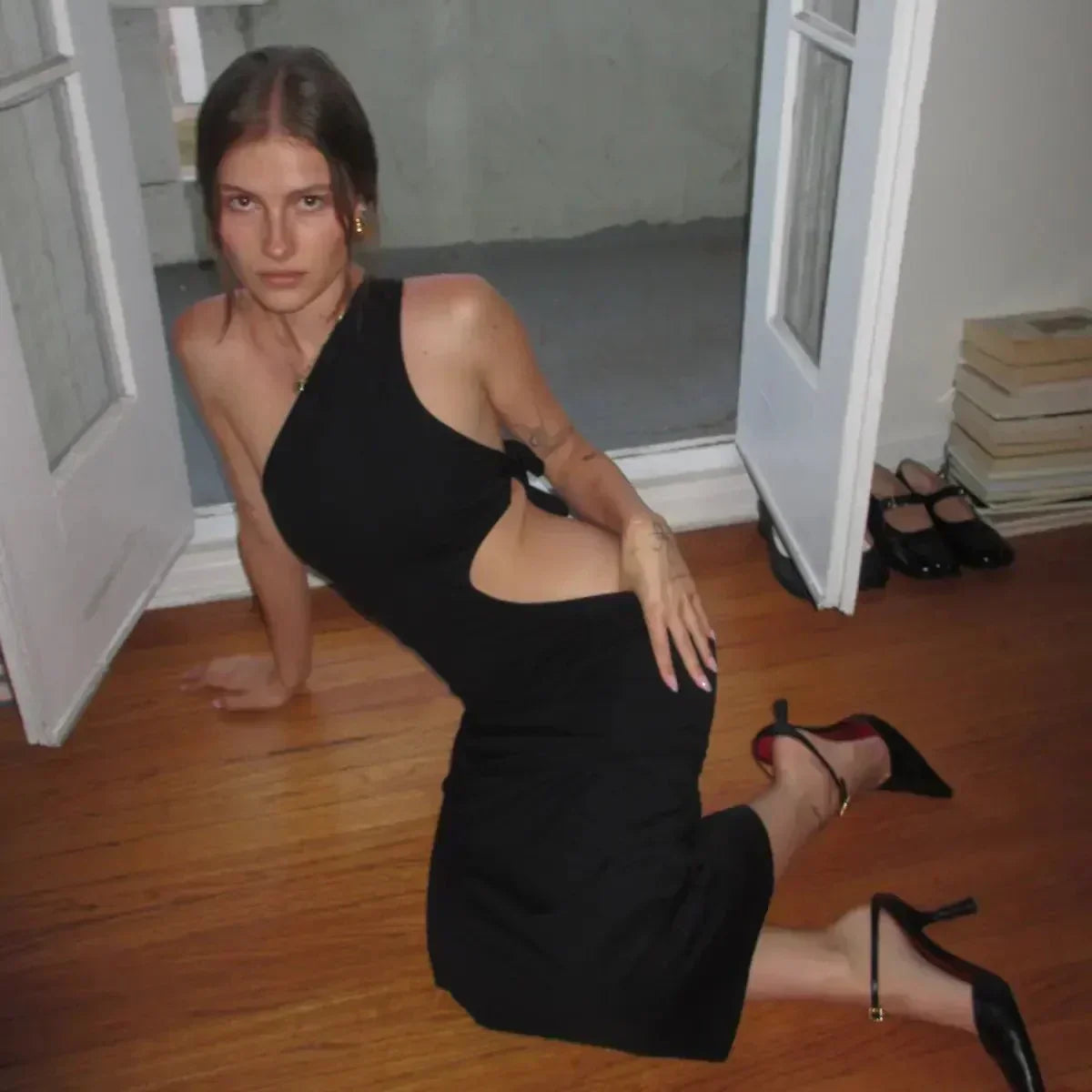Sleeveless midi dress in black with one-shoulder design and side cutout detail styled with black heels.
