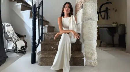 Style maxi dress in elegant white with a one-shoulder design, worn by a woman seated on marble steps indoors.