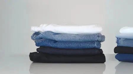 Low-rise denim jeans stacked in a neat pile showcasing different washes from black to white.