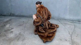 Stylish winter outfits featuring a luxurious long brown fur coat worn outdoors against a textured concrete background