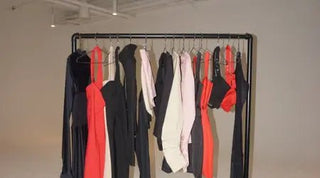 Catsuit capsule collection displayed on a garment rack with bold, minimal pieces in black, red, and neutral tones.
