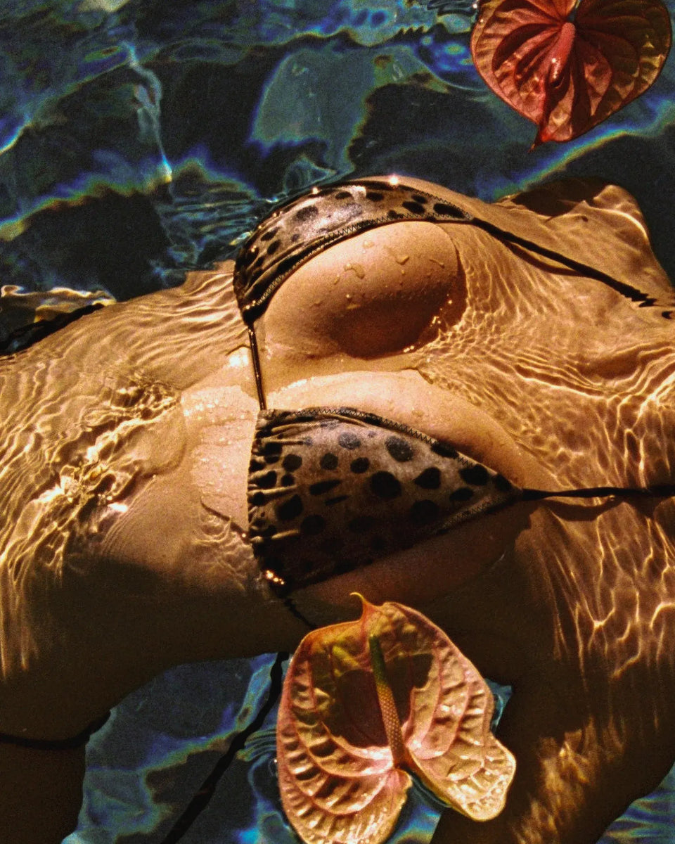 Leopard bikini top worn by woman floating in a pool with tropical flowers and sunlight reflecting on water.