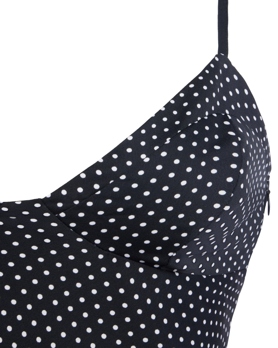 Polka dot mini dress with white dots on black fabric and thin shoulder straps in a close-up detail view.
