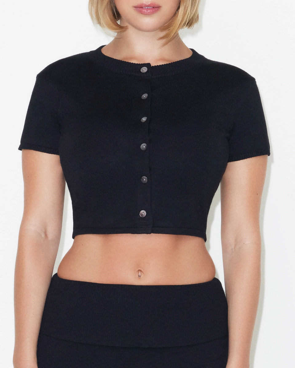 Black knit button up crop top with short sleeves and front buttons, shown worn with a matching waistband skort.